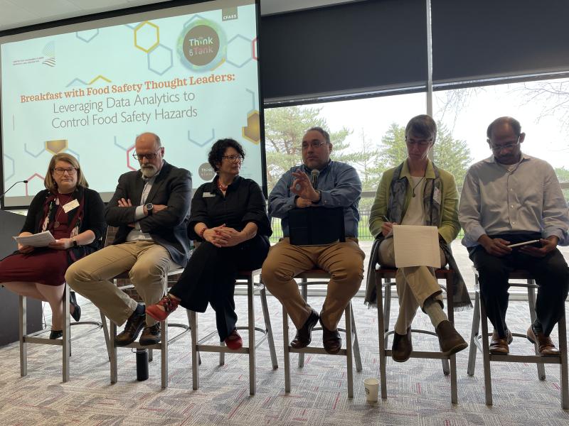 a row of 6 seated panelists presenting in a conference room. 