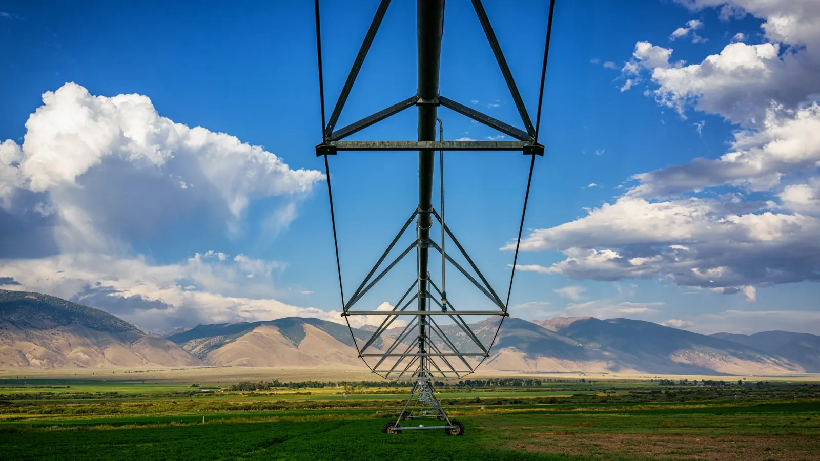An irrigation system sits in an agriculture field under a blue sky with mountains in the far background.