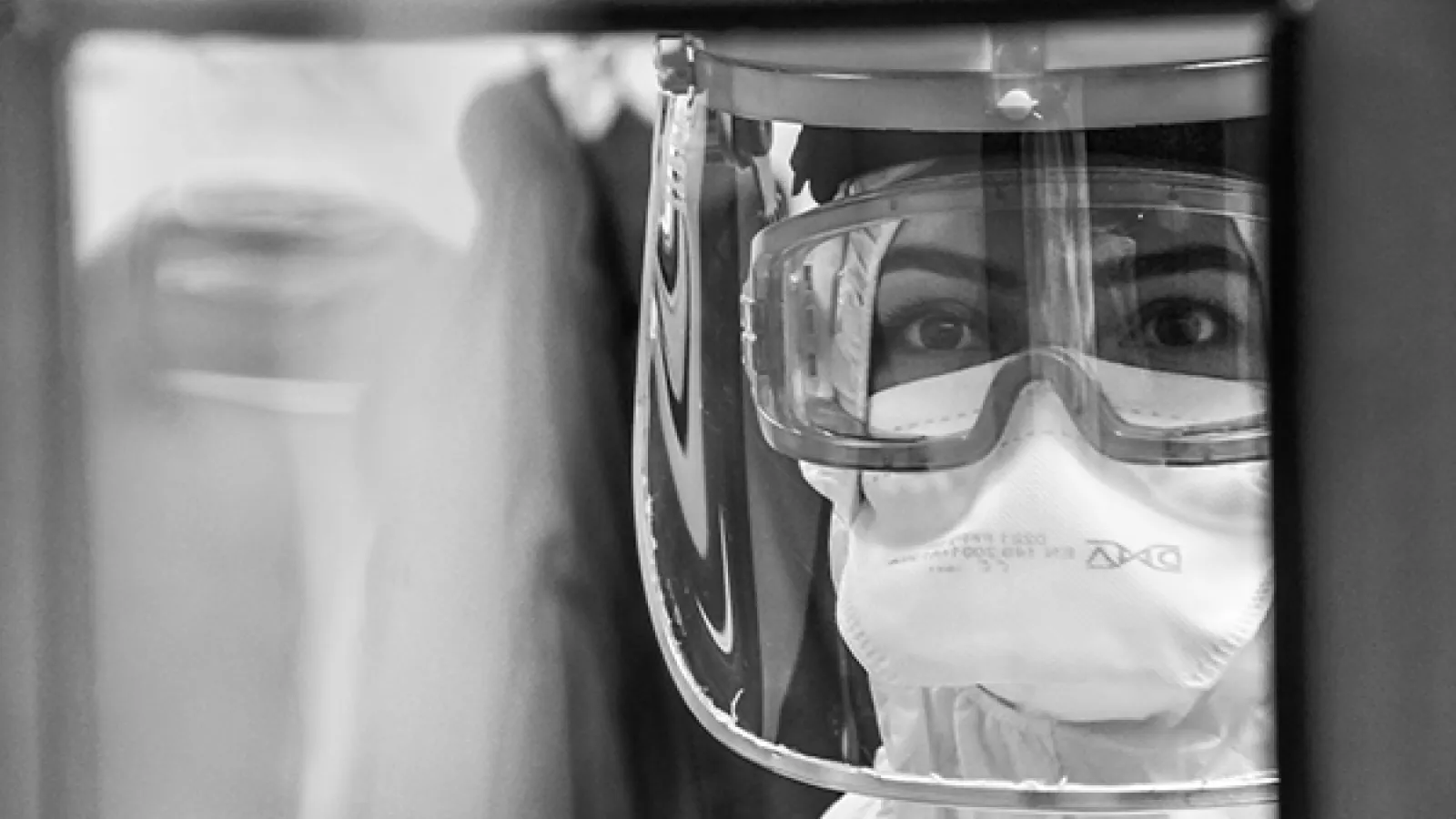 A nurse in PPE looking through a window