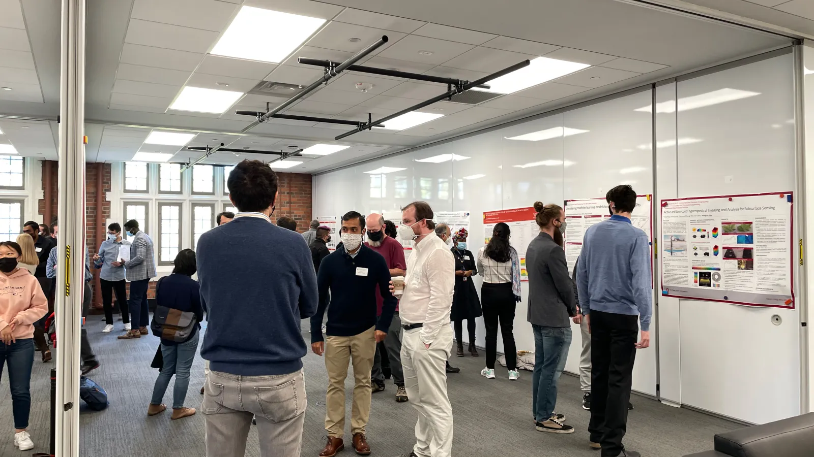 A photo of a room with research posters displayed on the walls and people discussion the posters