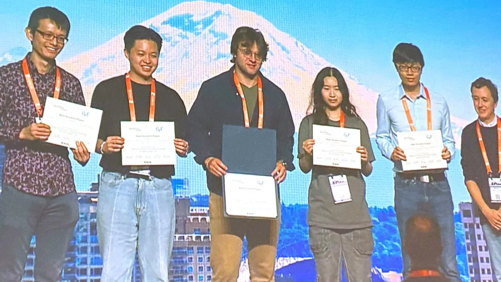 Faculty, students and staff stand on stage holding their award