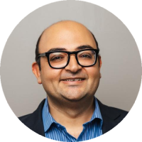Headshot of Dr. Faisal Mahmood, wearing glasses, a dark blazer, and a blue shirt, against a neutral background.