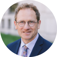 Headshot of Dennis Hirsch wearing glasses and a suit with a patterned tie, photographed outdoors.