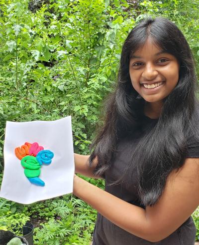 A Zoom image of a summer camp student outdoors holding a brain model she created