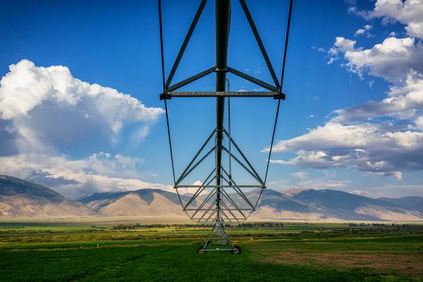An irrigation system sits in an agriculture field under a blue sky with mountains in the far background.