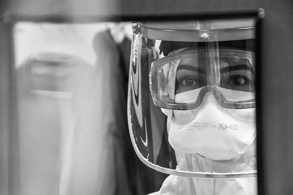 A nurse in PPE looking through a window