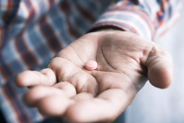 A photo of a Black man's hand holding a pill