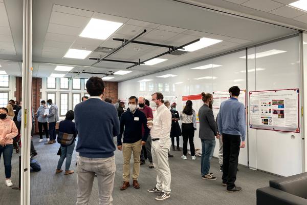 A photo of a room with research posters displayed on the walls and people discussion the posters
