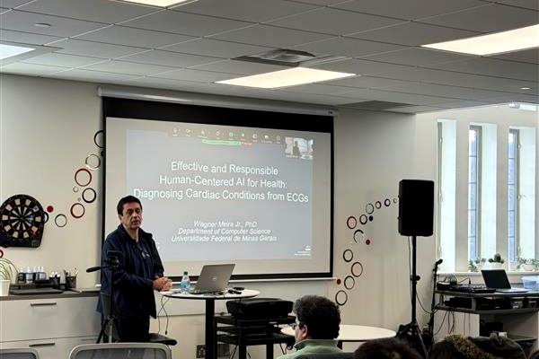 Wagner Meira Jr. presenting to an audience in Pomerene Hall with a projected slide on human-centered AI for health behind him.