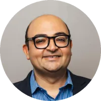 Headshot of Dr. Faisal Mahmood, wearing glasses, a dark blazer, and a blue shirt, against a neutral background.