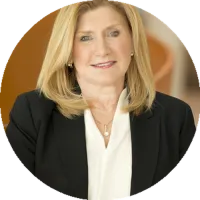 Headshot of JoAnn Stonier, wearing a black blazer and light blouse, against a softly blurred background.