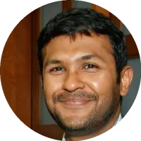 Headshot of Arnab Nandi wearing glasses and a collared shirt with a jacket, smiling against an indoor background.