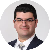 Headshot of Dr. Zachi Attia wearing glasses, a suit, and a tie against a neutral background.