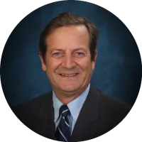 Headshot of David Noever wearing a suit and tie, smiling against a blue studio background.