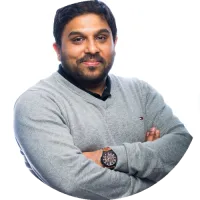 Headshot of Rajeev Chhajer smiling slightly, wearing a gray sweater and watch, against a white background.